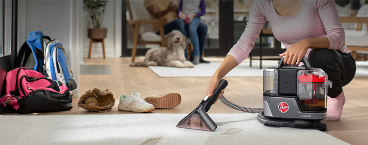 A woman cleans up muddy paw prints on her entryway rug while her dog watches
