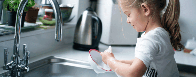 A little girl washes her bowl at the kitchen sink