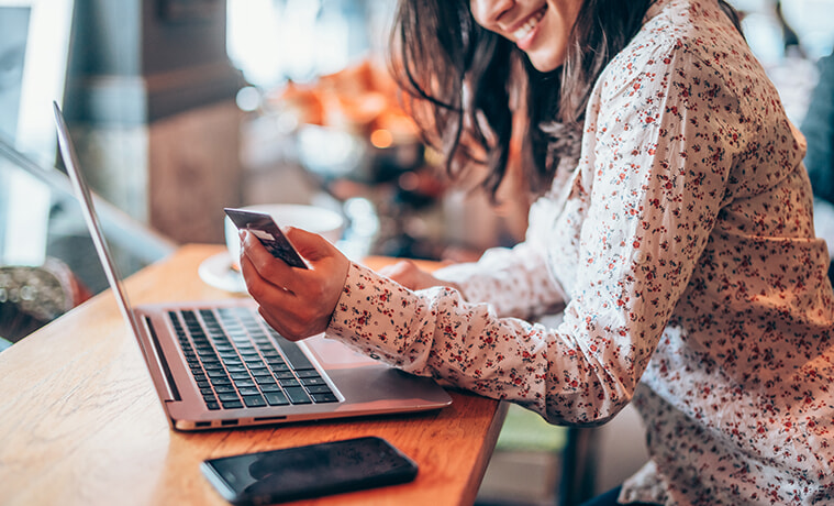 A woman in a cafe does some online shopping on her smartphone and laptop 