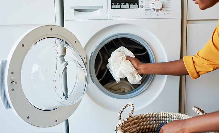 Closeup shot of a woman placing a white lace cloth into a front loading washing machine in her laundry