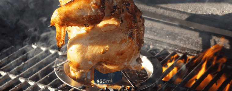 A can sits inside the cavity of a chicken cooking on a hot BBQ