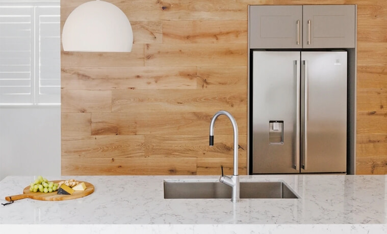 A silver kitchen tap matches the silver kitchen appliances in a timberfilled kitchen