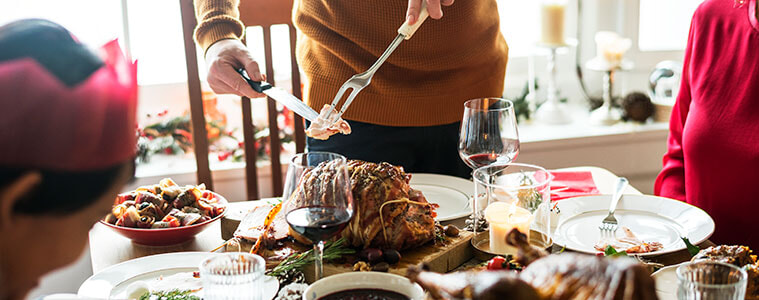 A family sits around the dining table on Christmas Day as the dad carves and serves the Christmas ham
