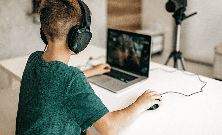 A boy wears a gaming headset while playing a video game on his gaming laptop