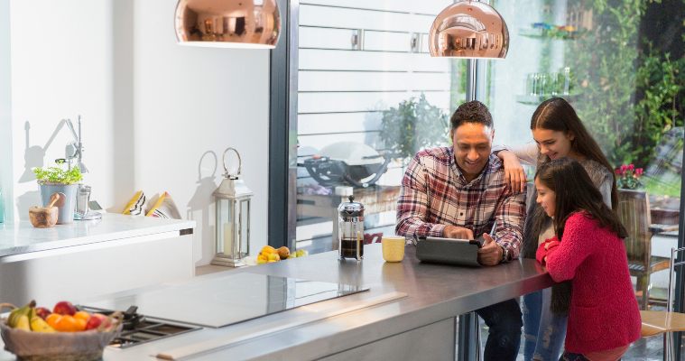 Family in kitchen looking at EOFY deals on an iPad