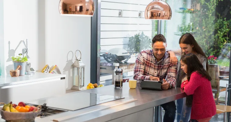 Family in kitchen looking at EOFY deals on an iPad