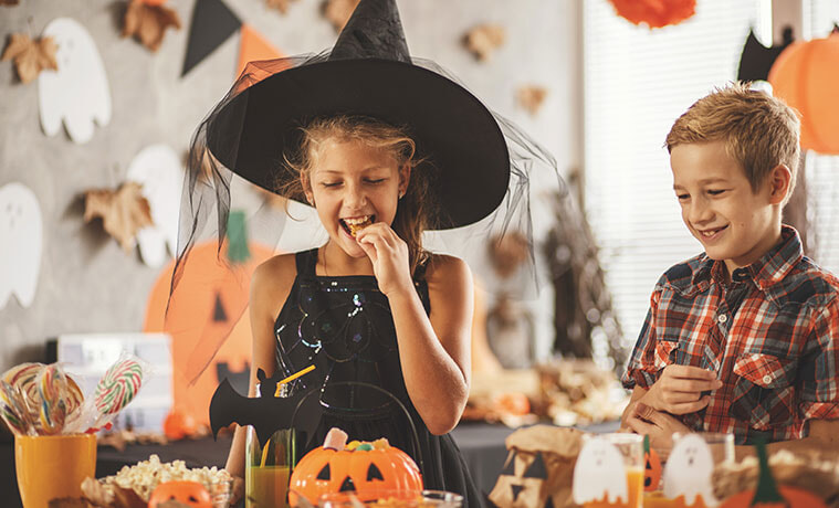 Boy and girl in Halloween costumes eat spookythemed snacks at a party