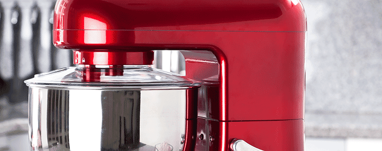 A red stand mixer on a kitchen bench with cake ingredients such as eggs butter and sugar