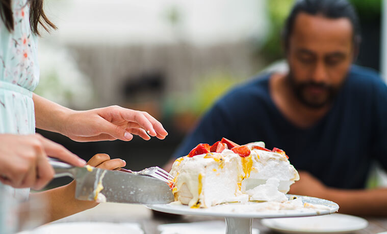 A woman serves slices of homemade pavlova as family members sit around an outdoor table