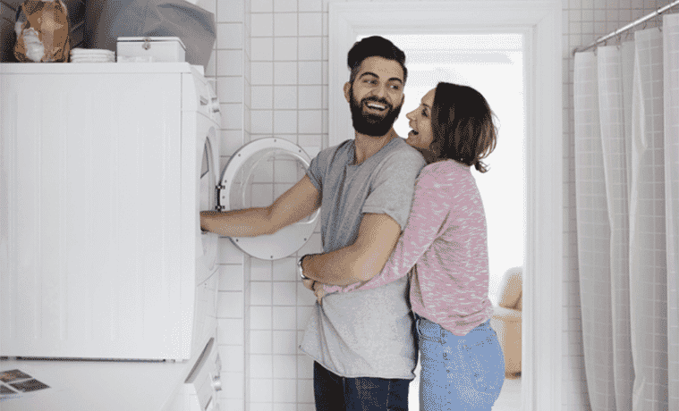 Young couple emptying the dryer together pleased at their new purchase which has a higher star rating
