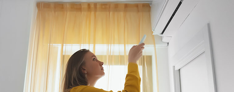 A woman aims a remote control at her wallmounted air conditioner
