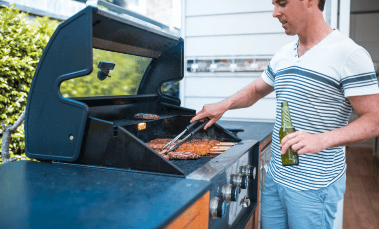 A man cooks sausages on the builtin barbecue on his outdoor deck