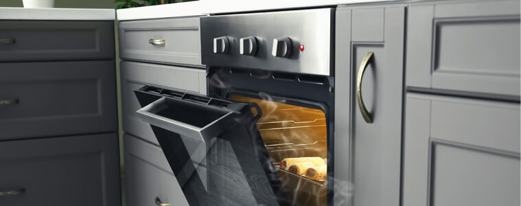 Steam escapes out of an open steam oven with freshly cooked sausage rolls inside