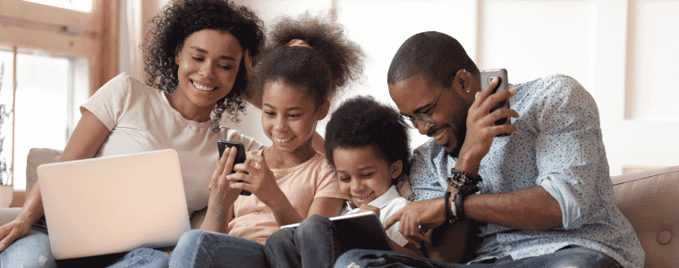 A family sitting on their couch happily looking at their phones and laptops 