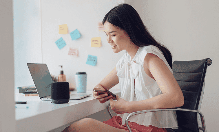 Young woman works from home with her smart assistant speaker and her portable laptop