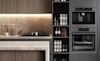 Modern kitchen detail with dark timber cabinetry natural stone island bench and splashback and builtin coffee machine and wall oven in a black finish 