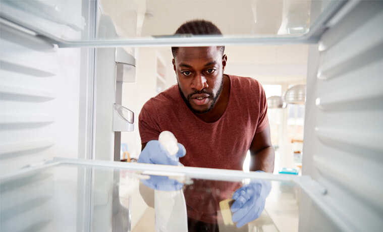 A man sprays and wipes down the interior of his fridge