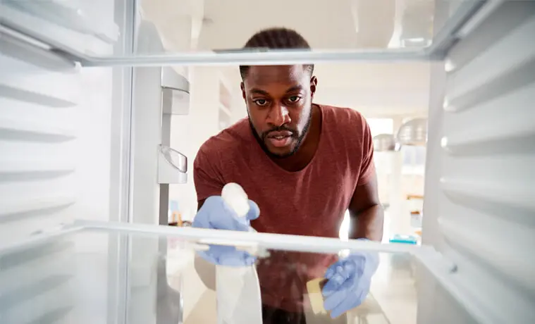 A man sprays and wipes down the interior of his fridge