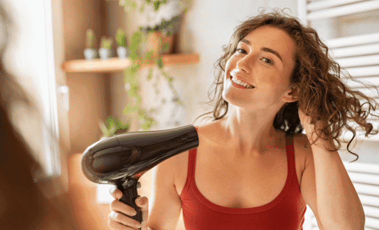A woman dries her hair with a hair dryer while looking in the mirror