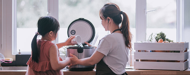 Mother and daughter together at the kitchen bench making rice in a rice cooker