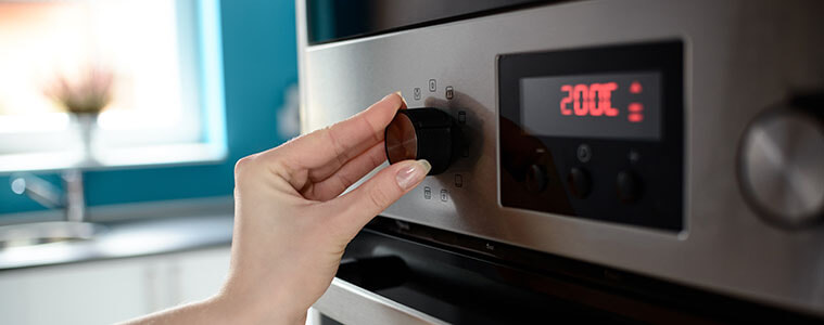Closeup of a womans hand turning the knob on a wall oven to adjust the temperature