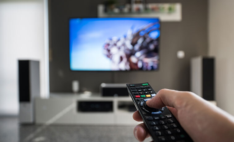 A man points his TV remote at a big screen TV mounted on the wall in his living room 