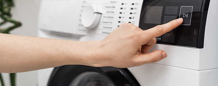 A person presses the start button on their washing machine