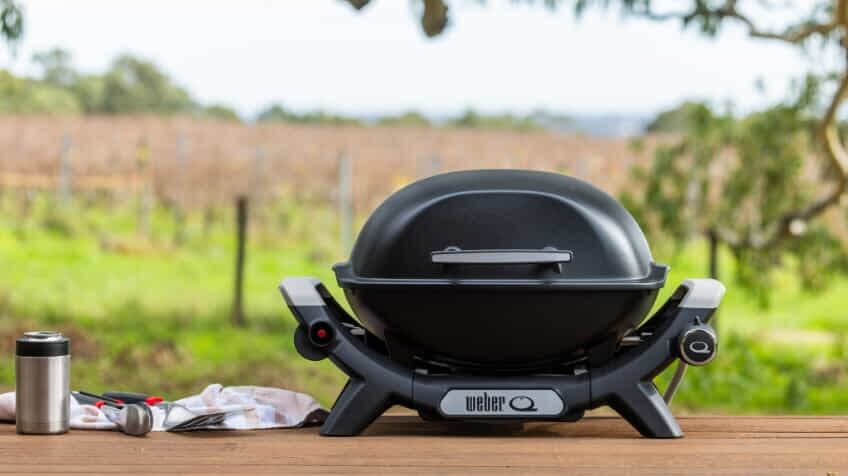 A black Weber Baby Q sits on a picnic table at a vineyard