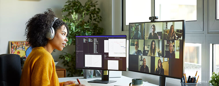 A female entrepreneur sitting at a desk with two monitors and a keyboard leads a business meeting on a video call