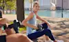 A woman in a park uses the Hyperice Hypervolt massage gun on her leg in a park