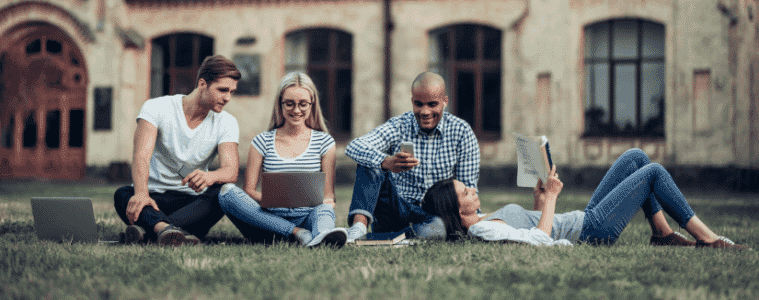 Four Students using laptops phones and reading books in a park