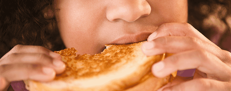 Closeup of a young girl eating a toasted sandwich