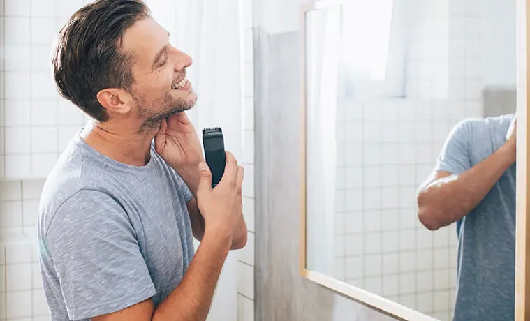 Man shaves with an electric shaver in the bathroom mirror
