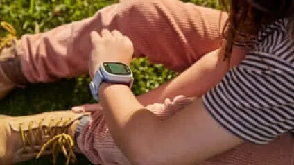 A young girl sitting on the grass looking at her Spacetalk Adventurer 2 smartwatch