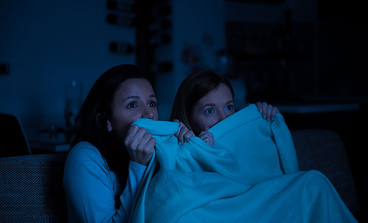 Teenage girls hold a blanket up to their face while watching a scary movie