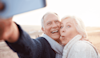 Lovely older couple are taking a selfie on the beach with their mobile phone The husband is smiling and the wife is making a funny face