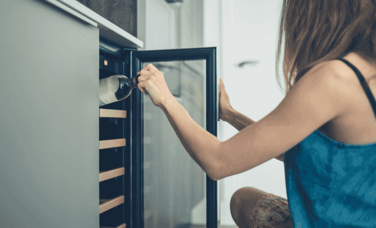 A young woman is getting a bottle of white wine from her wine cooler at home