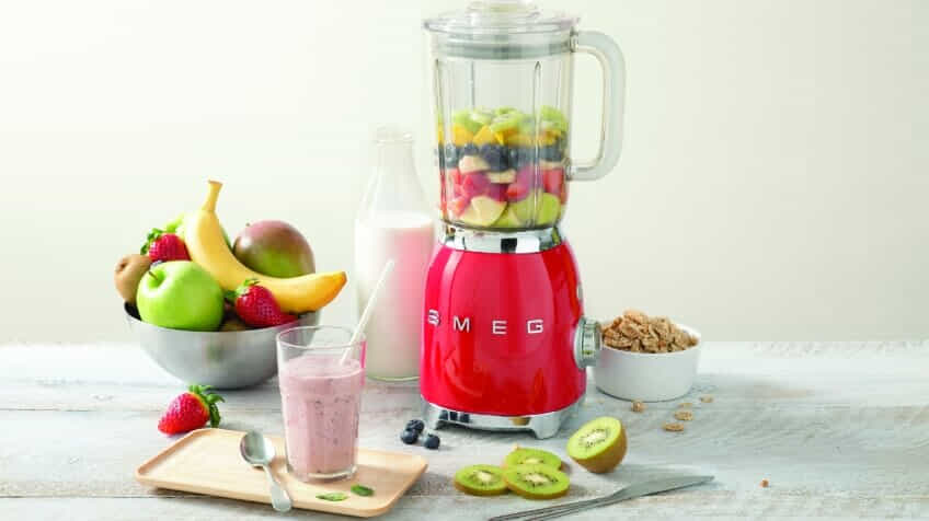 A red Smeg retro blender filled with fruit for a smoothie