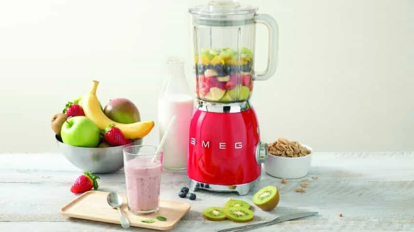 A red Smeg retro blender filled with fruit for a smoothie