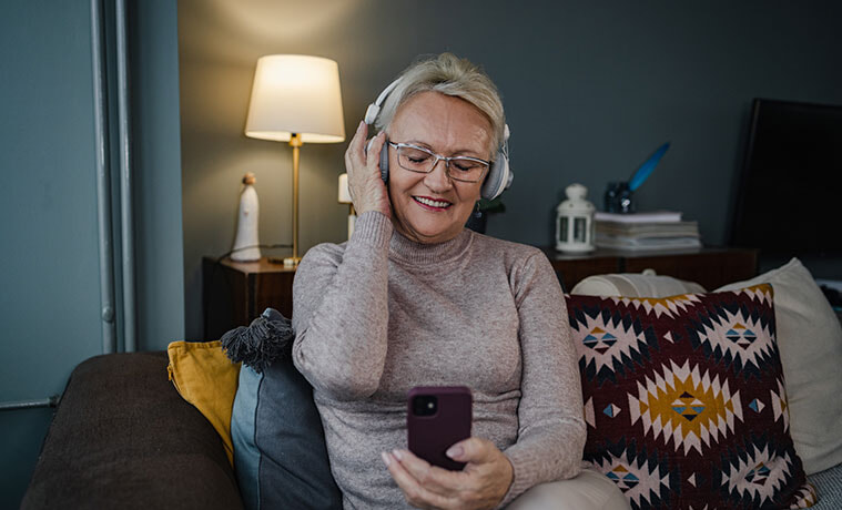 Senior woman on a couch listening to music streamed from her smartphone through white headphones