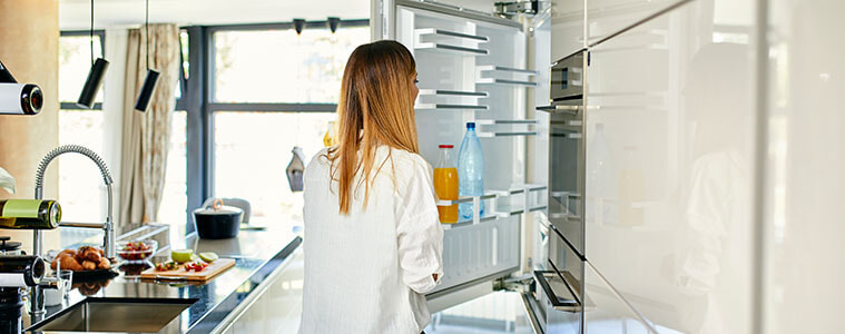 A woman opens the door of an integrated fridge in her modern and lightfilled kitchen