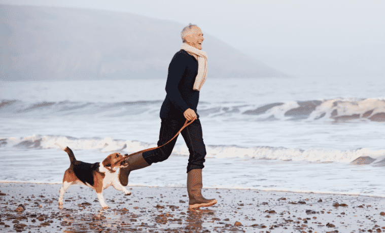 a man running along the beach in winter with his dog wearing a scarf and boots 