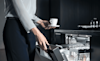 A woman opens her dishwasher to stack her empty cup and saucer