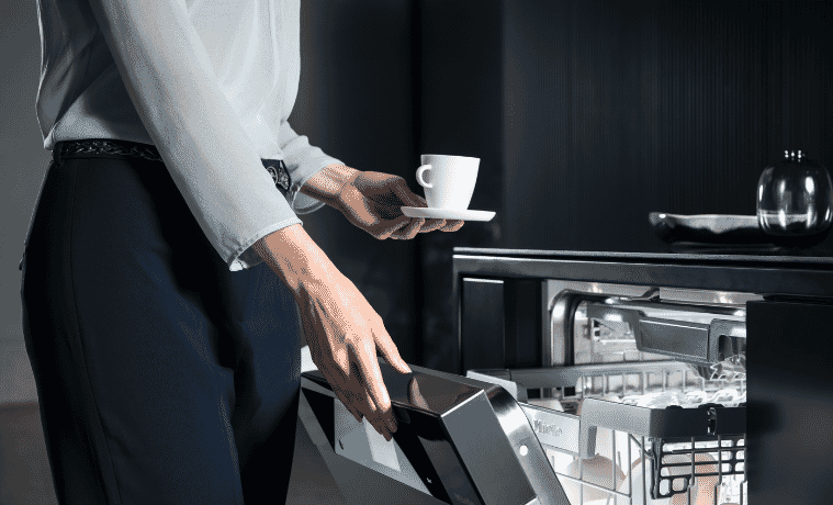 A woman opens her dishwasher to stack her empty cup and saucer