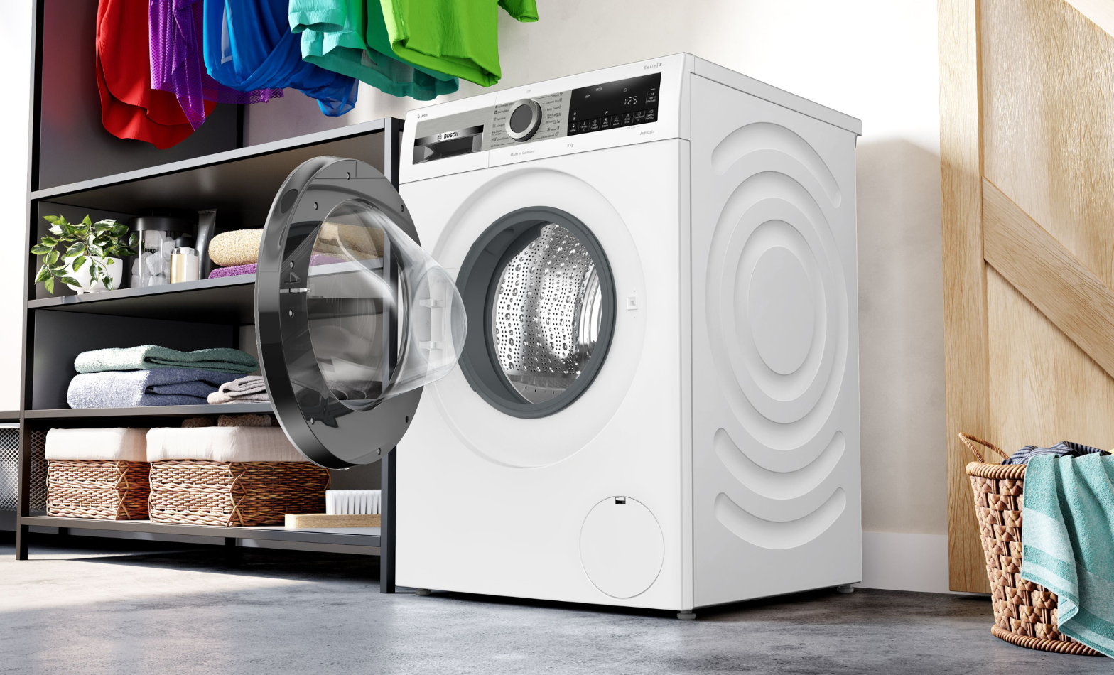 A Bosch washing machine sits next to a small basket with a blue shirt hanging over the edge of  the basket