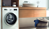 A Bosch washing machine sits next to a small basket with a blue shirt hanging over the edge of  the basket