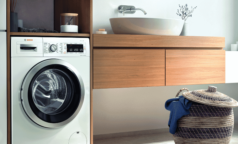 A Bosch washing machine sits next to a small basket with a blue shirt hanging over the edge of  the basket