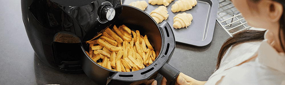 A woman prepares French fries in a black air fryer