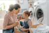 Mother and daughter laugh and smile while sitting on the floor in their laundry with a basket of fresh clothes