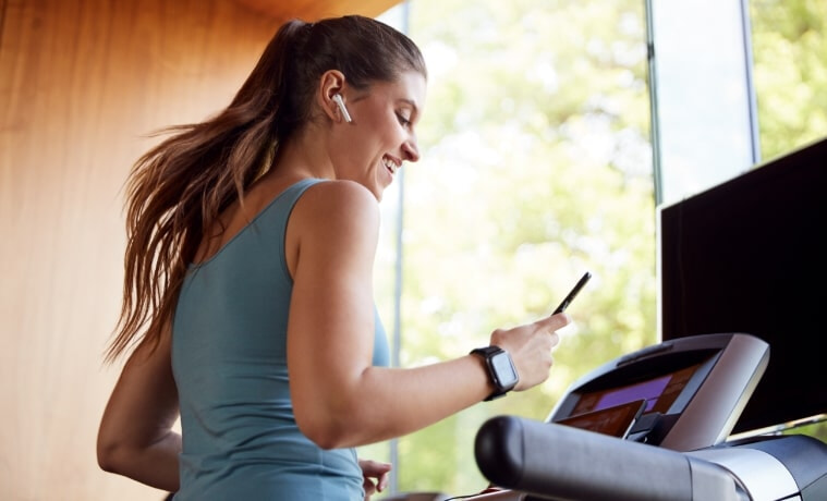 Woman smiling whilst using a treadmill and her smartphone